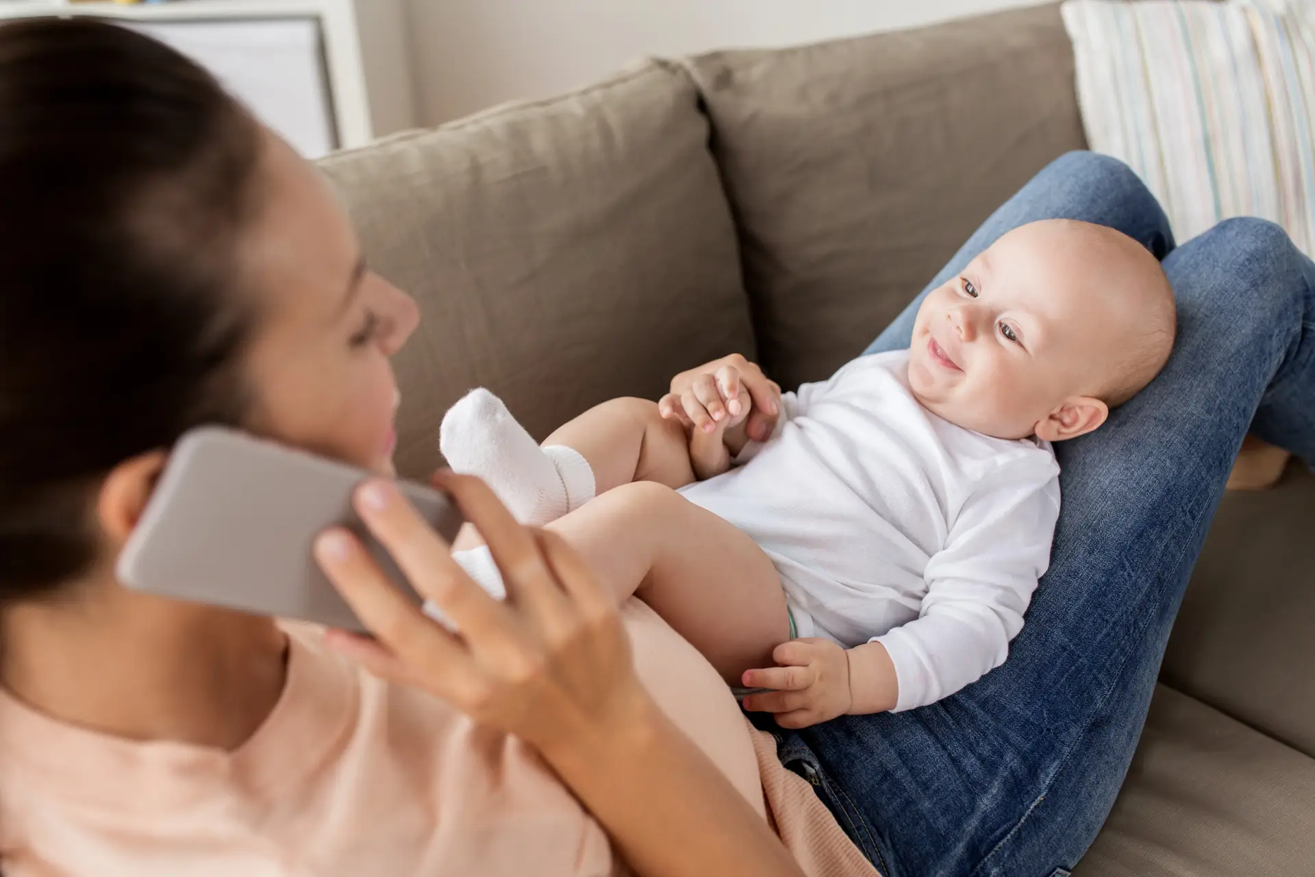 Smiling new mom holding her baby while talking on the phone in her kitchen